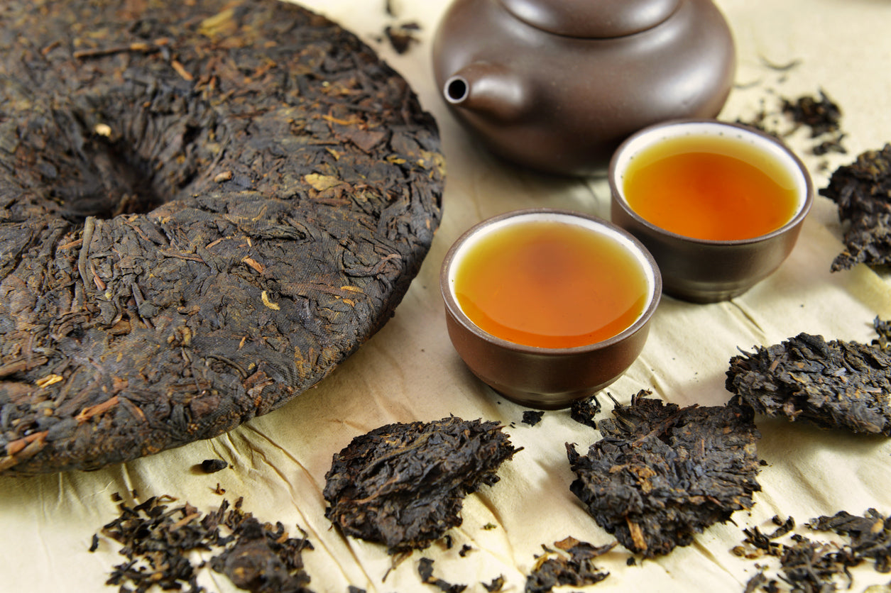 A pu erh tea cake with two cups and a kettle