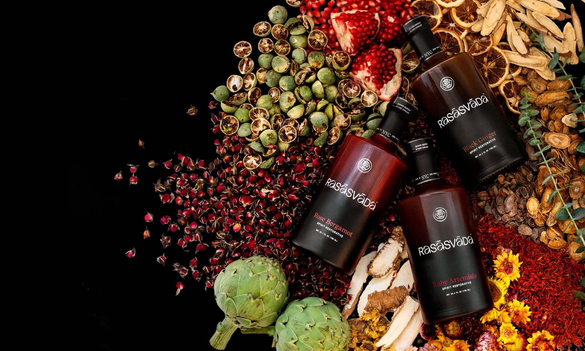 Bottles of Ruby, Rose, and Black Ginger with visible branding on a bed of dried herbs, spices, pomegranate, and artichoke.