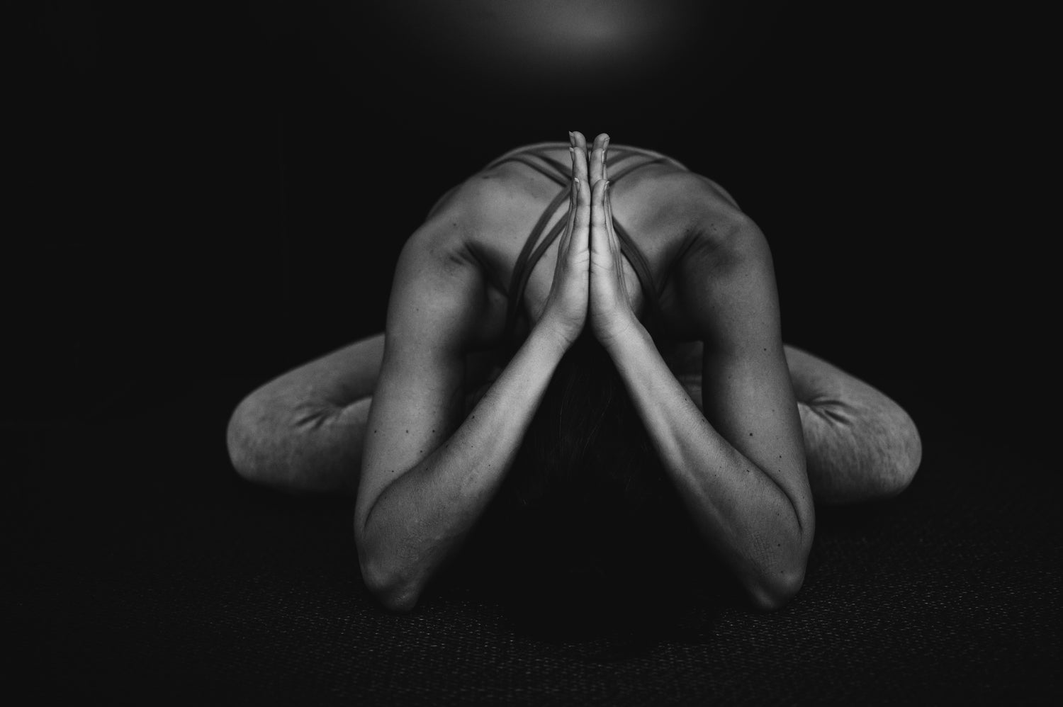 Black and white image of a person in a yoga pose with hands pressed together on a dark background
