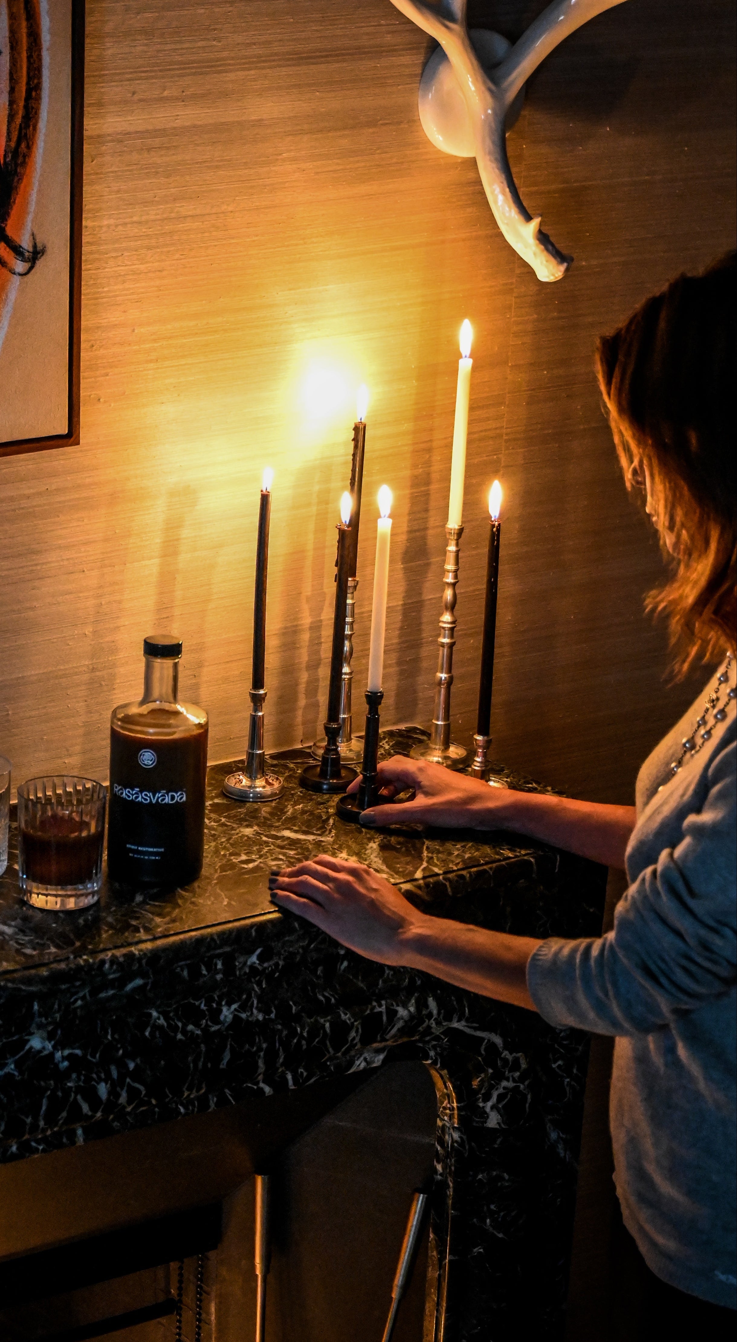 Person lighting candles on a bar counter with a bottle of Rasasvada and glassware.