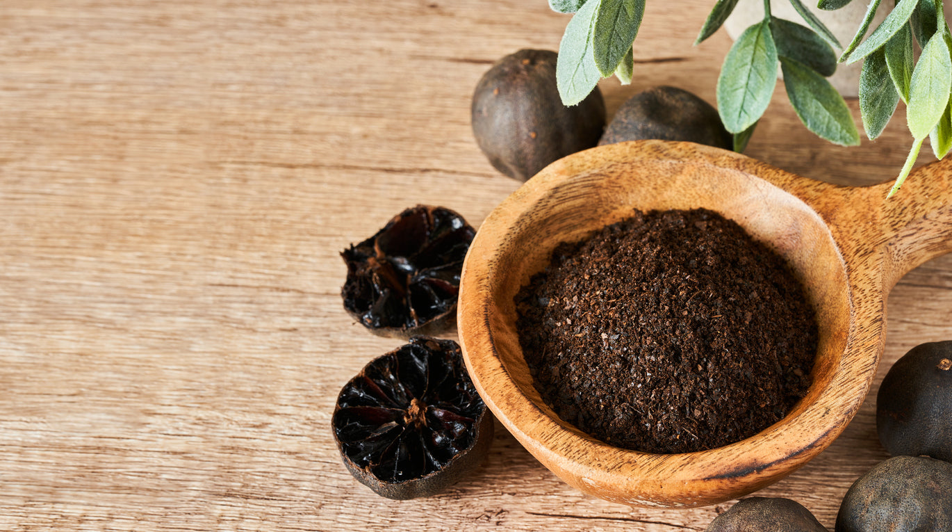 Wooden scoop filled with ground black seed and whole seeds on a wooden surface