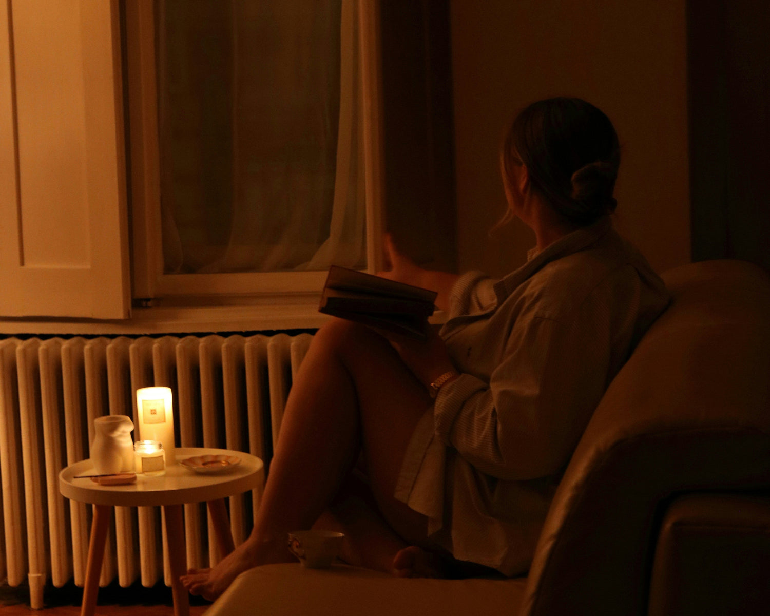 Person sitting on a couch in a dimly lit room with a candle and radiator visible.