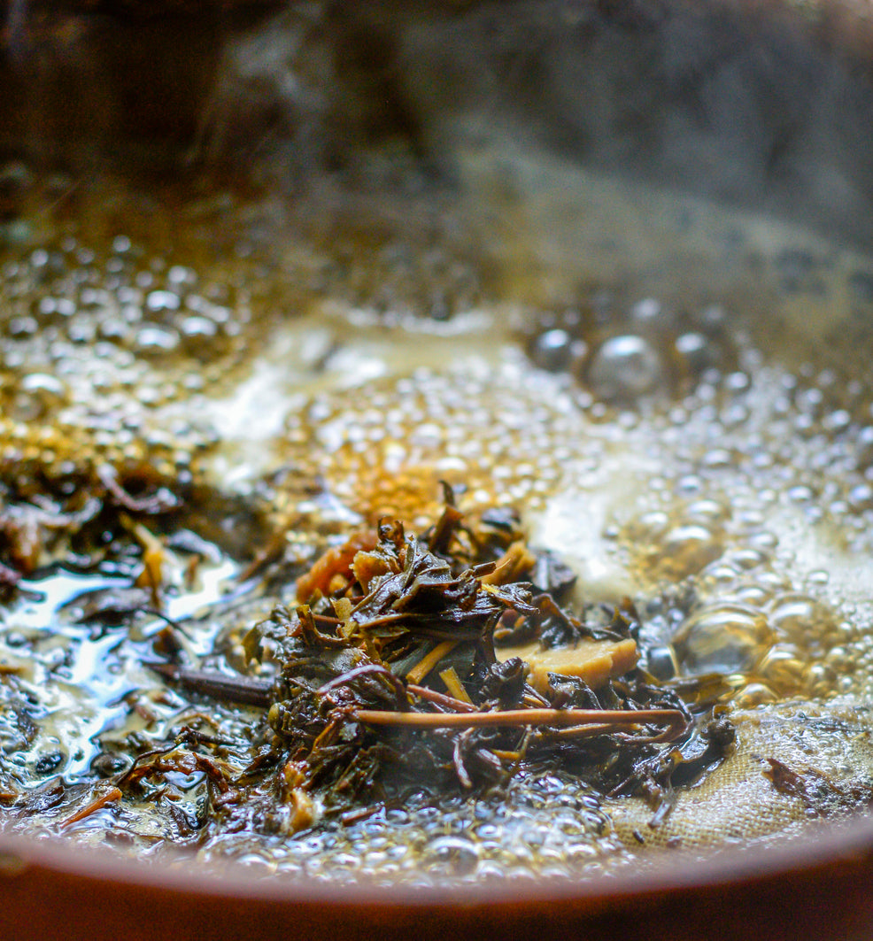 Close-up of loose-leaf tea leaves steeping in hot, bubbling water inside a dark ceramic pot.